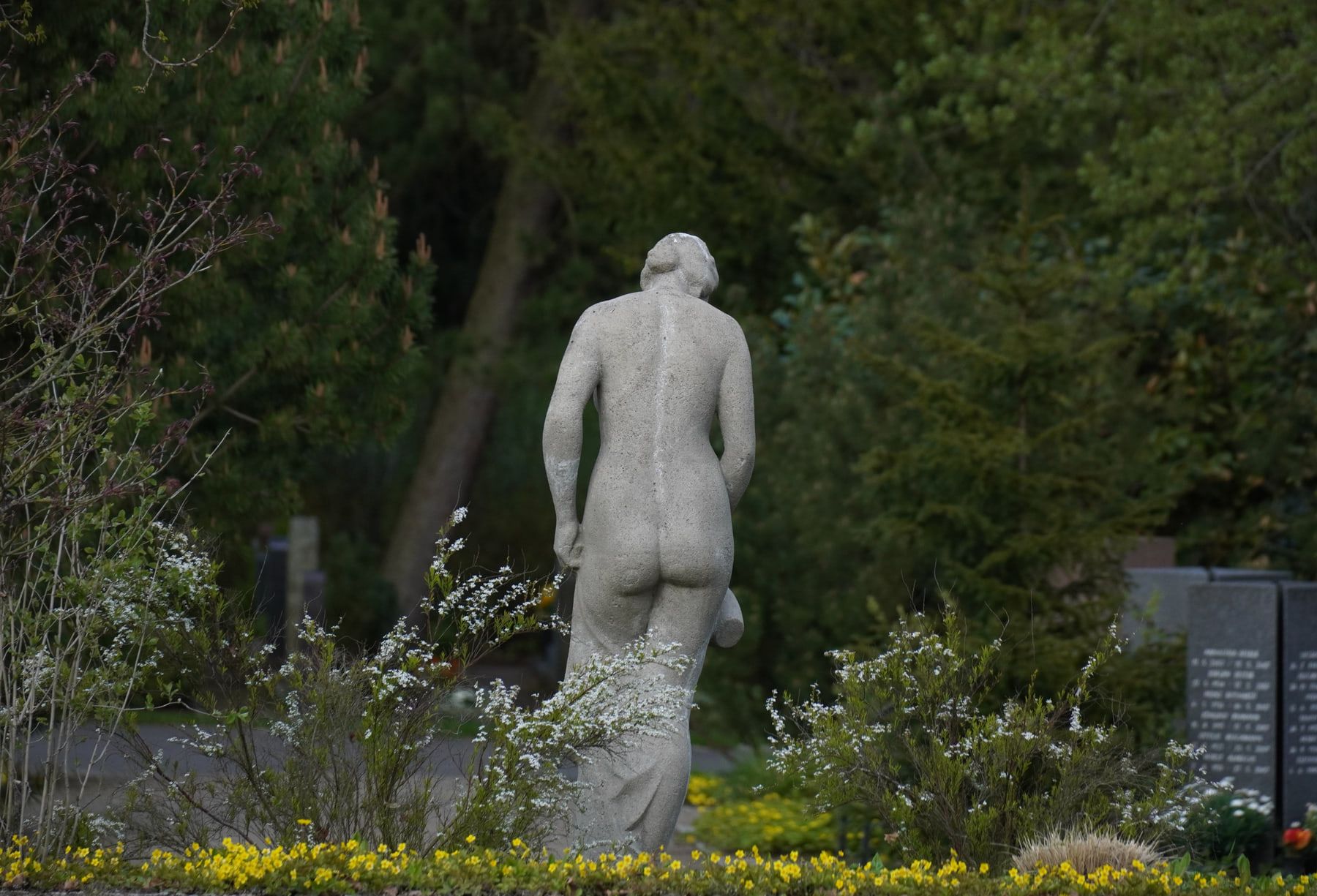 Kniende Steinfigur am Brunnen zwischen bepflanzten Grabstätten auf Hauptfriedhof Erfurt